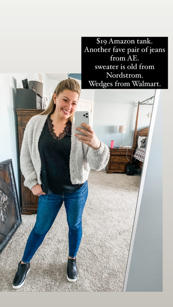 A young woman smiles white looking at her phone in the mirror. she is wearing a fuzzy gray cardigan, black lacey tank, medium wash blue jeans, and black and white sneaker platforms. the text on the photo says ' $19 amazon tank. another fave pair of jeans from AE. sweater is old from nordstrom. wedges from Walmart.'